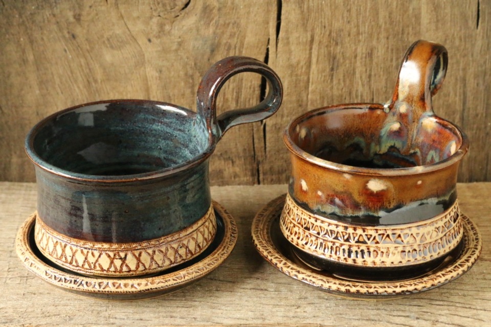 Zwei Rasierseifenschalen in graublau und rostrot mit Henkeln stehen nebeneinander - jeweils mit Unterteller. Alle 4 Teile haben gestempelte Muster - dunkel (Manganspinell) auf hellem Grund.